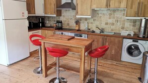 A compact kitchen with wooden cabinets, a built-in dishwasher, a sink, and a washing machine. - Beautiful River-front Villa with Natural Pool & Aircon (Sorède)