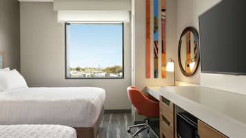 Quarto de hotel com duas camas, uma escrivaninha, uma cadeira, televisão de tela plana, uma janela grande e vista para a cidade.
