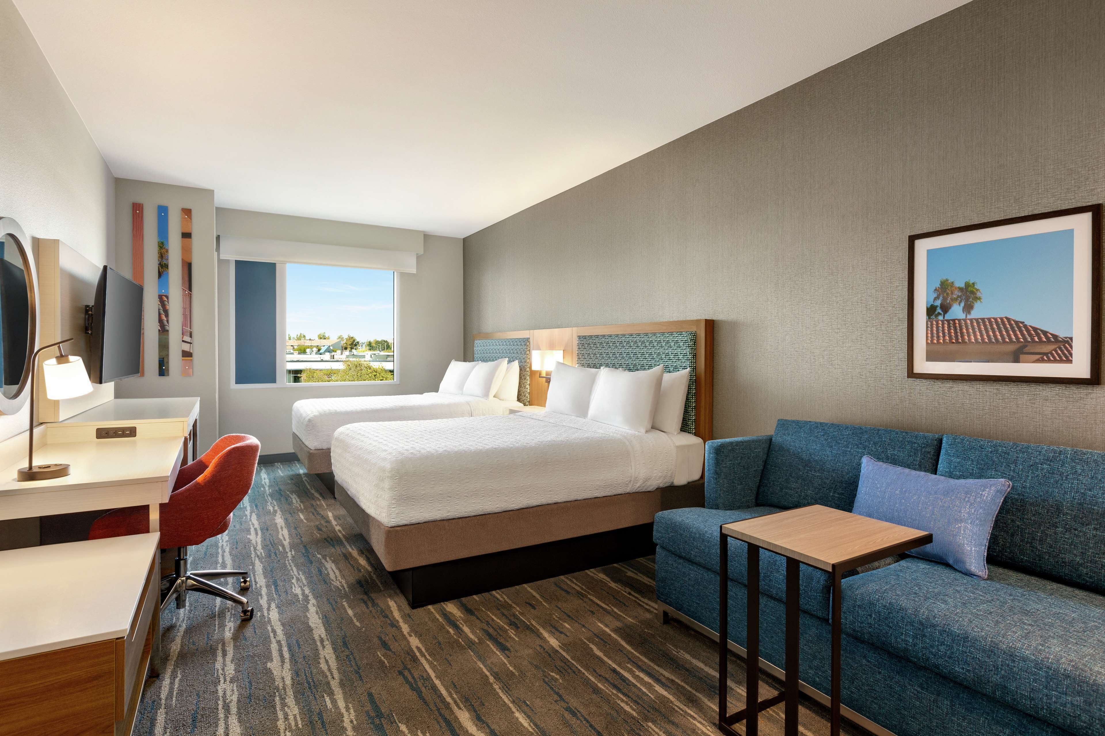 A hotel room with two beds, a desk, a chair, a sofa, and a small table.