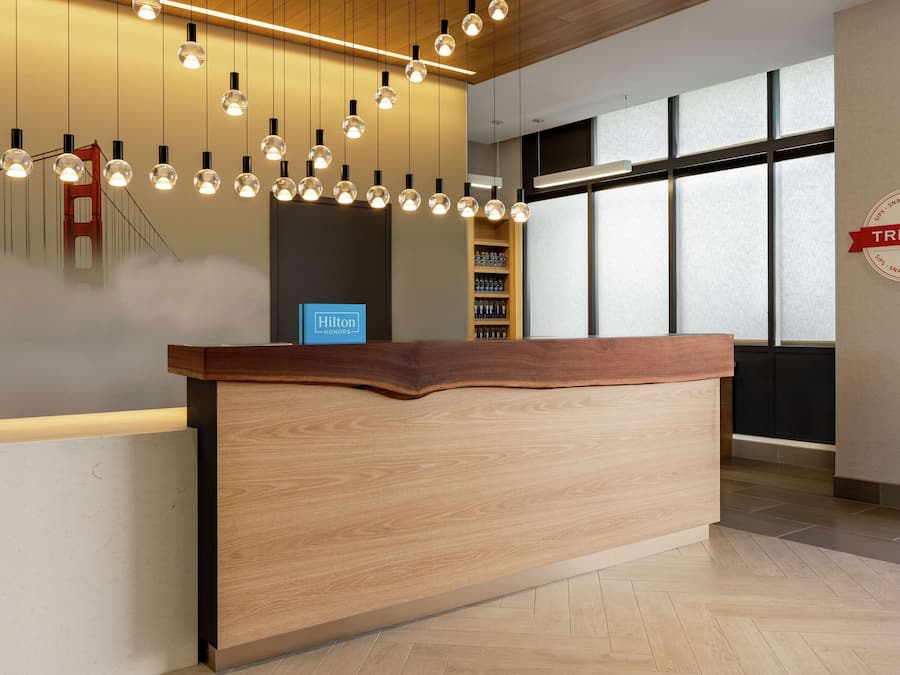 Una moderna reception di hotel con un bancone in legno, lampade pendenti, un minibar e vista sul Golden Gate attraverso ampie finestre.