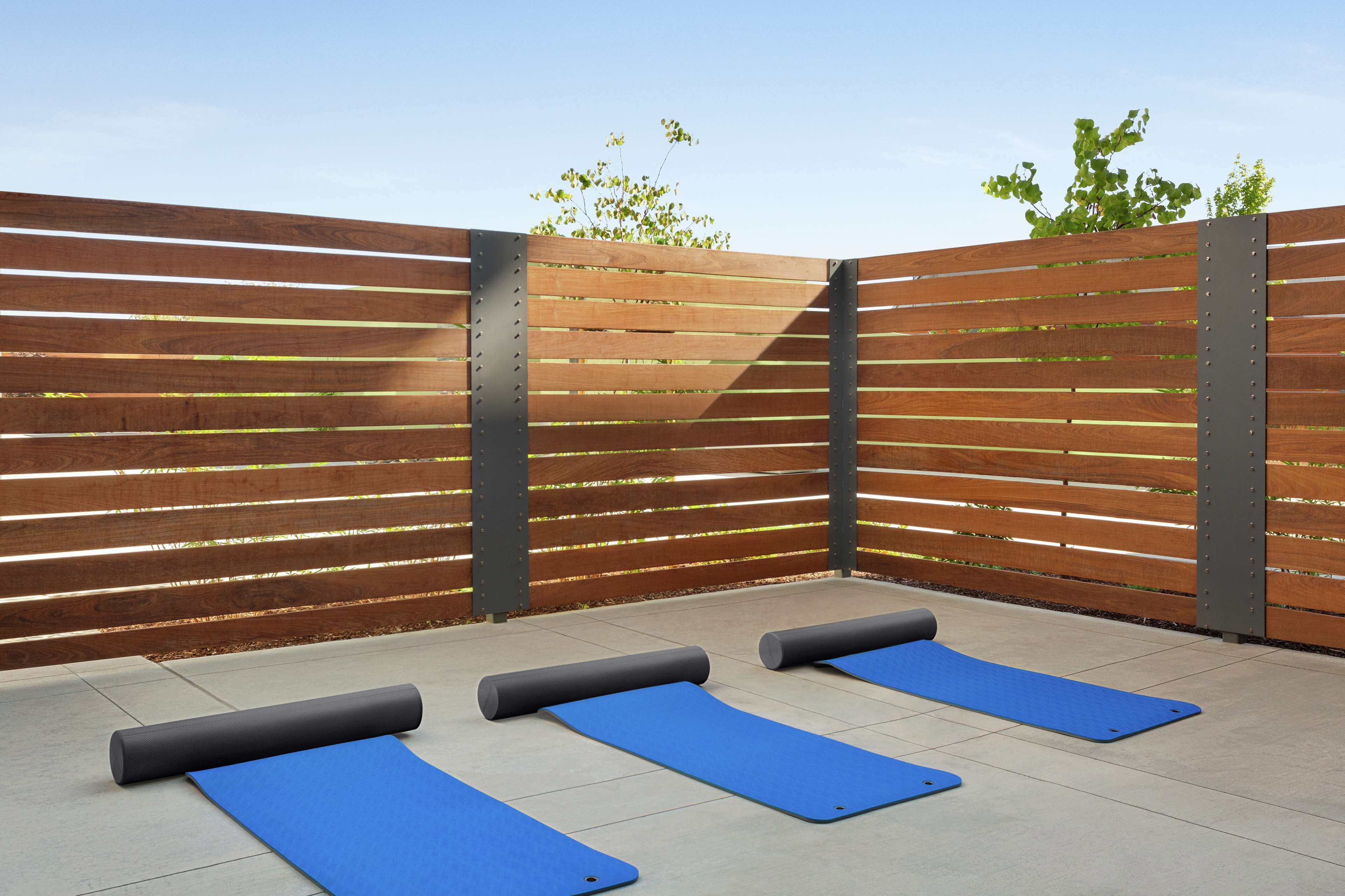 A wooden fence with metal supports, blue exercise mats, and a grey yoga mat on a tiled patio.
