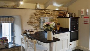 Een keuken met een stenen muur, een zwart aanrecht, witte kasten, een dubbele oven en een bloevas.