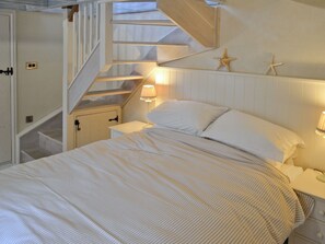 Une chambre à coucher avec un lit, des tables de chevet, une lampe, une étoile de mer en guise de décoration et un escalier.
