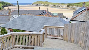 Een houten terras met een tafel en stoelen, met uitzicht op een strand en gebouwen.