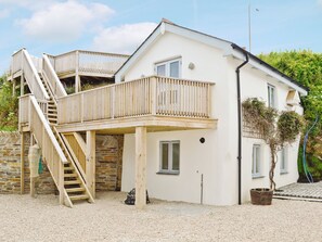 A two-story house with a wooden staircase leading to a balcony, a stone wall, and a small garden area.