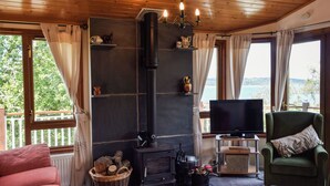 Interior acogedor de una cabaña con chimenea, televisor y vistas al exterior.