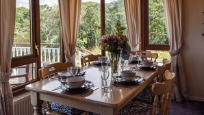 Mesa de comedor lista para cuatro personas, con sillas, un jarrón de flores y vista a zonas verdes al exterior.