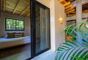 Una habitación con puerta corrediza de vidrio, un banco con cojines, una planta en maceta y ventana con vistas a follaje.