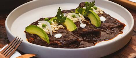 A plate of enchiladas with avocado and cheese garnish.