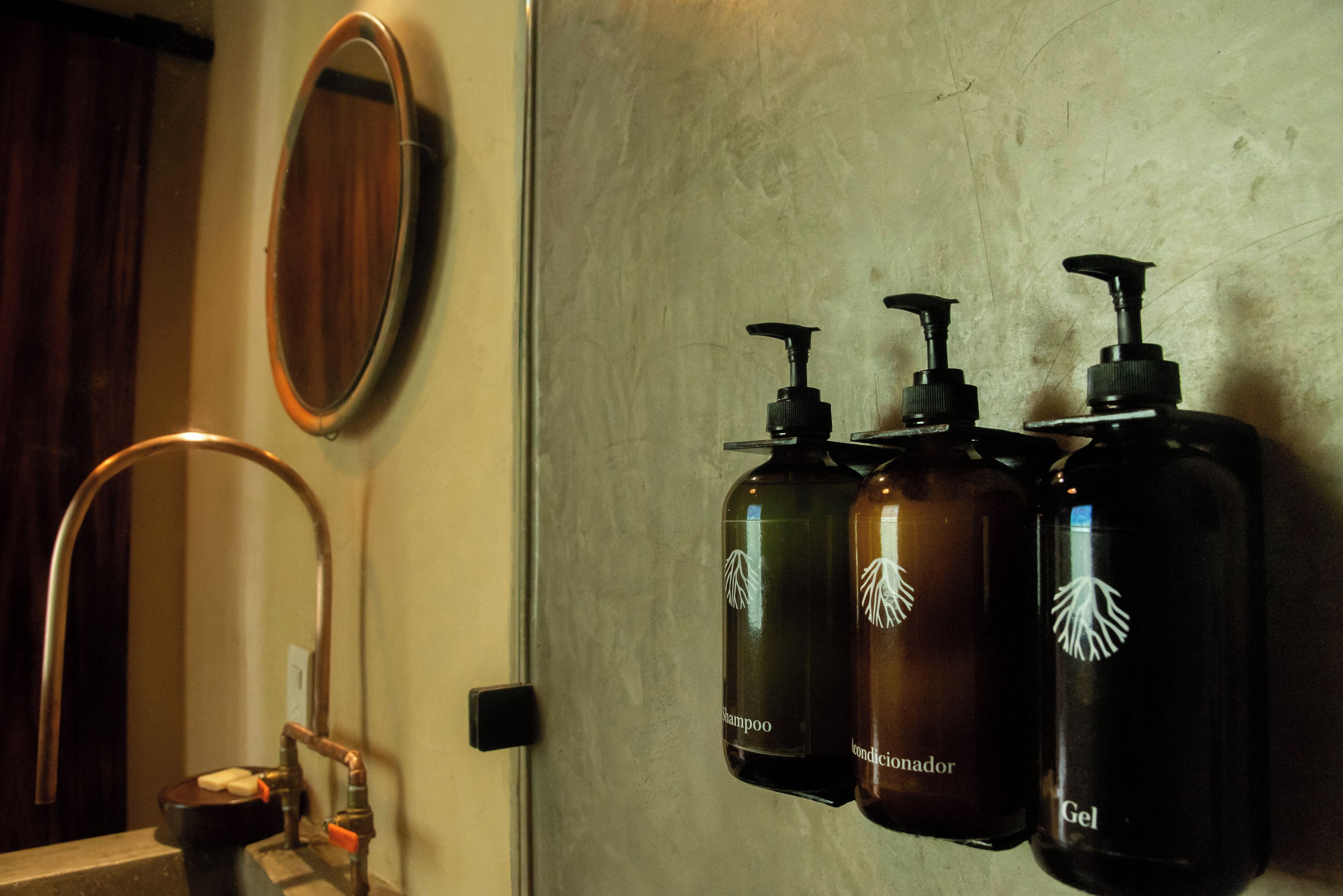A bathroom with a mirror, a sink, and three bottles of shampoo and conditioner.