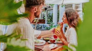 A couple dining at an outdoor table with a view of greenery and a building in the background.