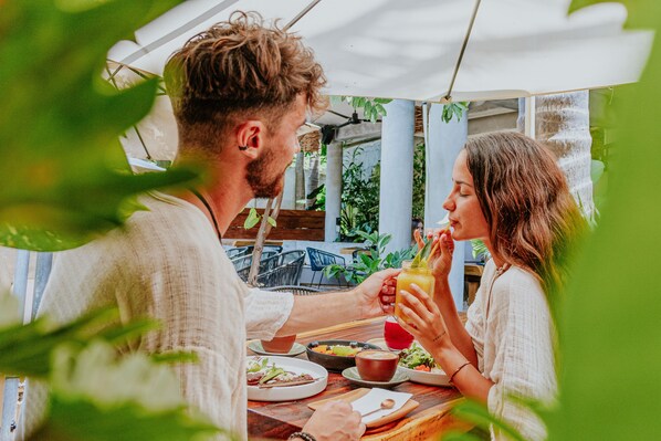 A couple dining at an outdoor table with a view of greenery and a building in the background.