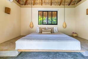 Un dormitorio con cama, ventana con vista a follaje y techo de paja.