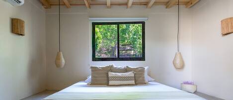 Un dormitorio con cama, dos lámparas colgantes, una ventana con vistas y una mesita de noche pequeña.