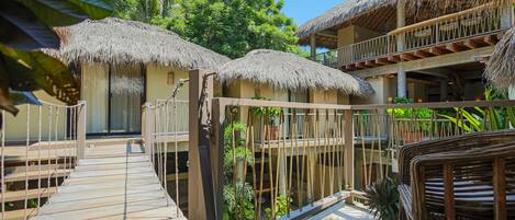 Un resort con estructuras de techo de paja, pasarelas de madera y un balcón con mobiliario de mimbre.