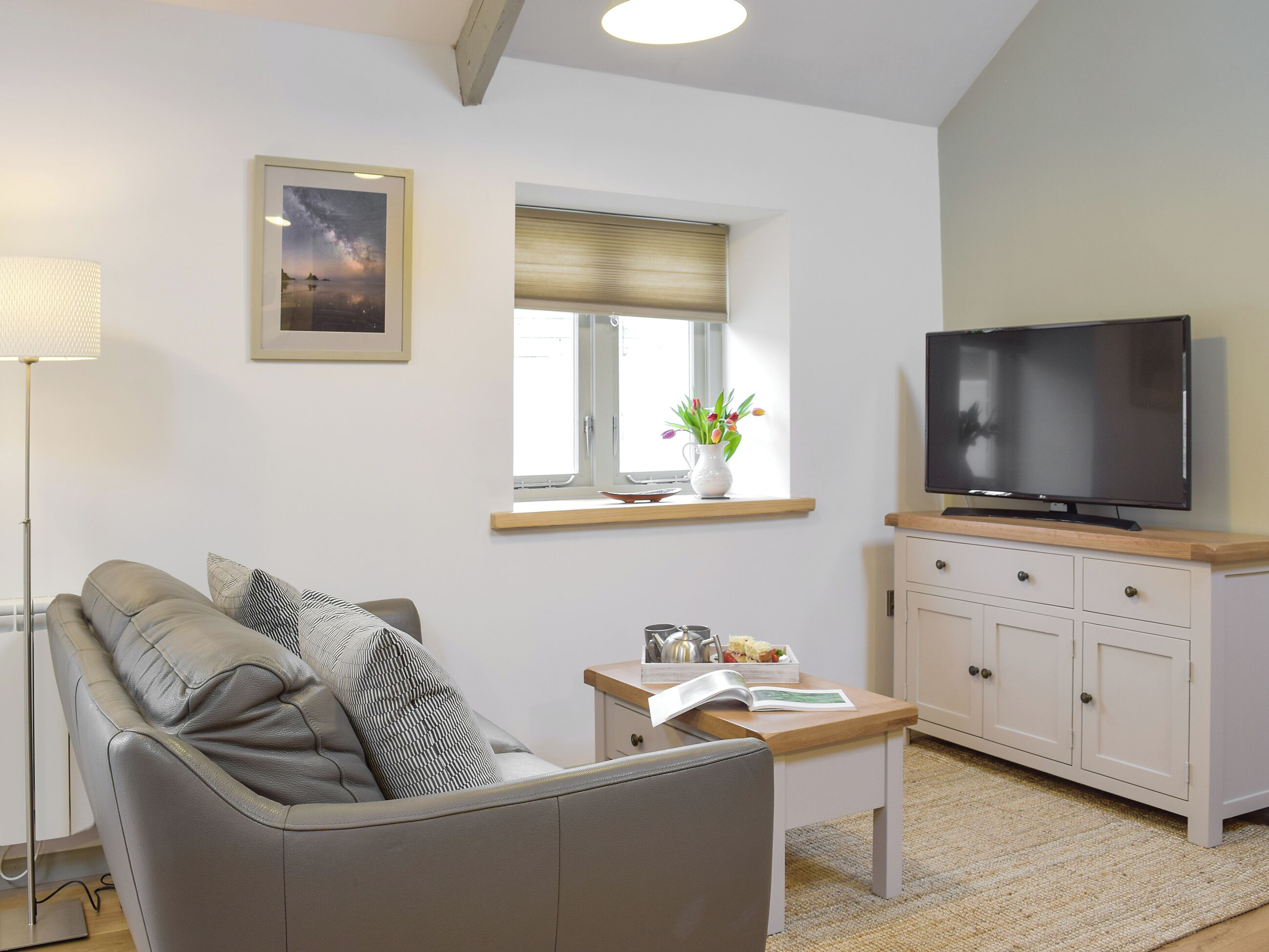 A living room with a sofa, a coffee table, a TV, a window with a view, and a lamp.