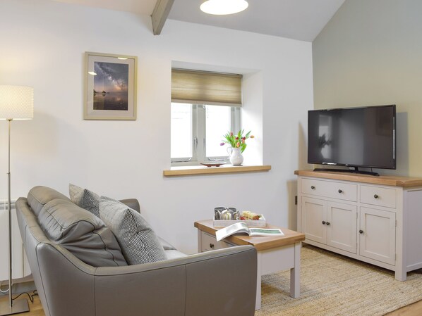 A living room with a sofa, a coffee table, a TV, a window with a view, and a lamp. - Honeysuckle Cottage-UKC3194 (Valast Hill, near Stackpole)