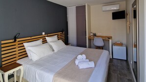 A hotel room with a bed, bedside table, desk, chair, and a small refrigerator. - le Cosy (Fréjus)