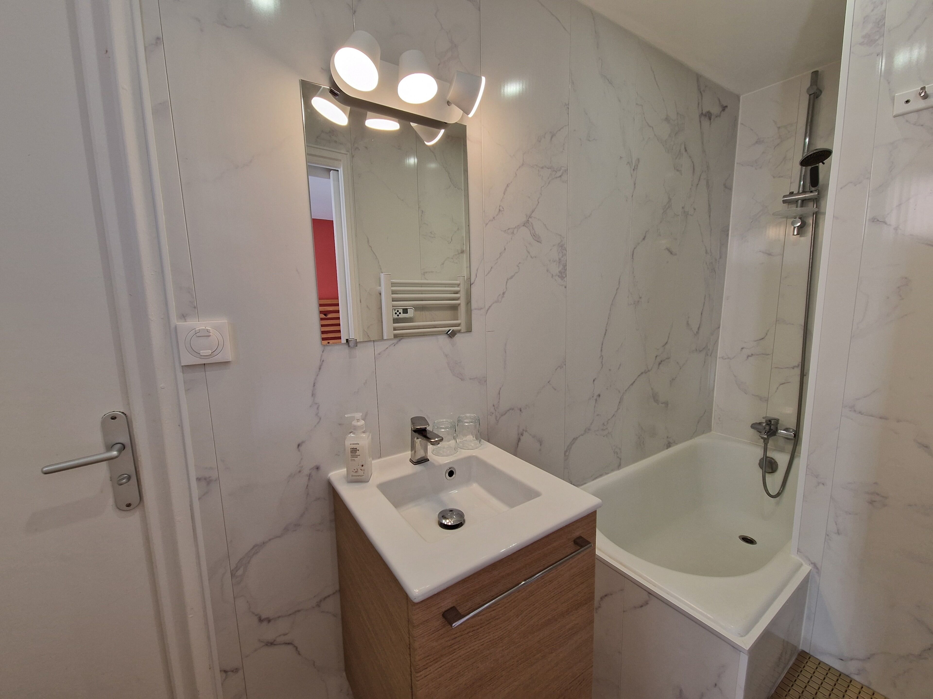 Un baño con pared de mármol, un lavabo, un espejo y una ducha.