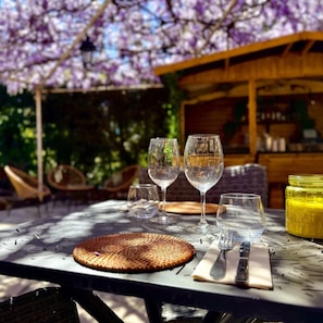 A table set outdoors with wine glasses, a woven placemat, cutlery, and a yellow container, likely containing a drink. - le Cosy (Fréjus)
