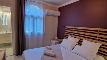 A hotel room with a bed, a nightstand, a window with curtains, an air conditioning unit, and a ceiling light fixture.