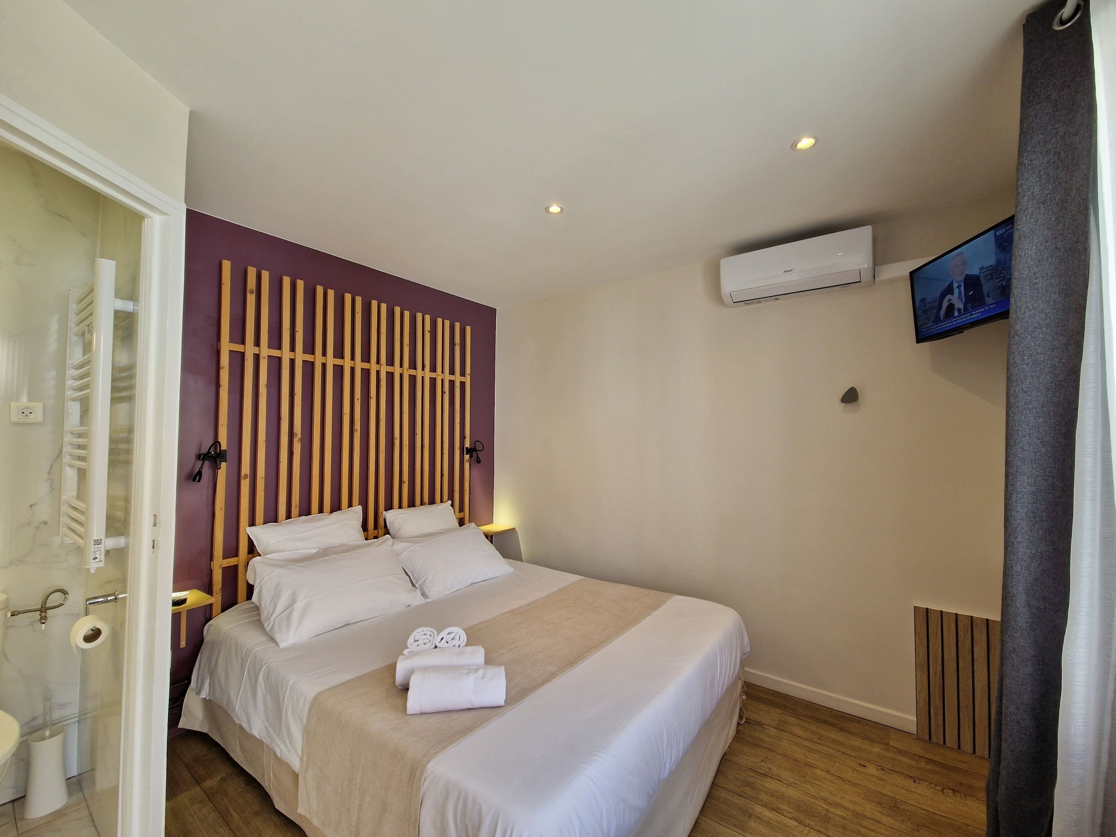 A hotel room with a bed, a wooden headboard, a TV, and an air conditioning unit.