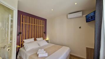 A hotel room with a bed, a wooden headboard, a TV, and an air conditioning unit.