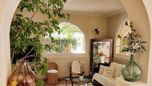 An interior with a stone-tiled floor, a sofa, a coffee table, a wicker chair, a vase with flowers, and a glass jar. - le Cosy (Fréjus)