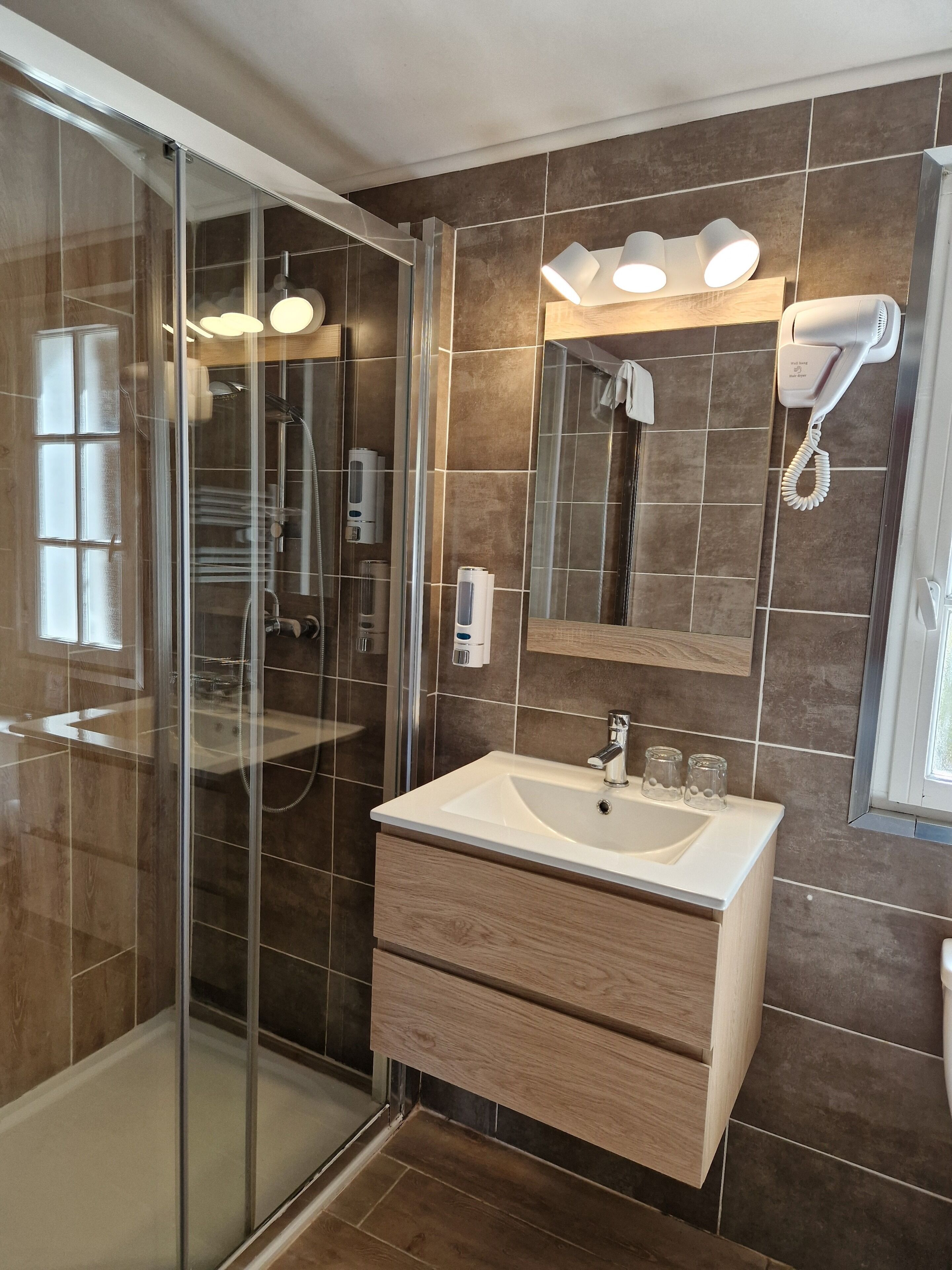 A modern bathroom with a glass shower enclosure, a vanity with a sink, and a mirror above it.