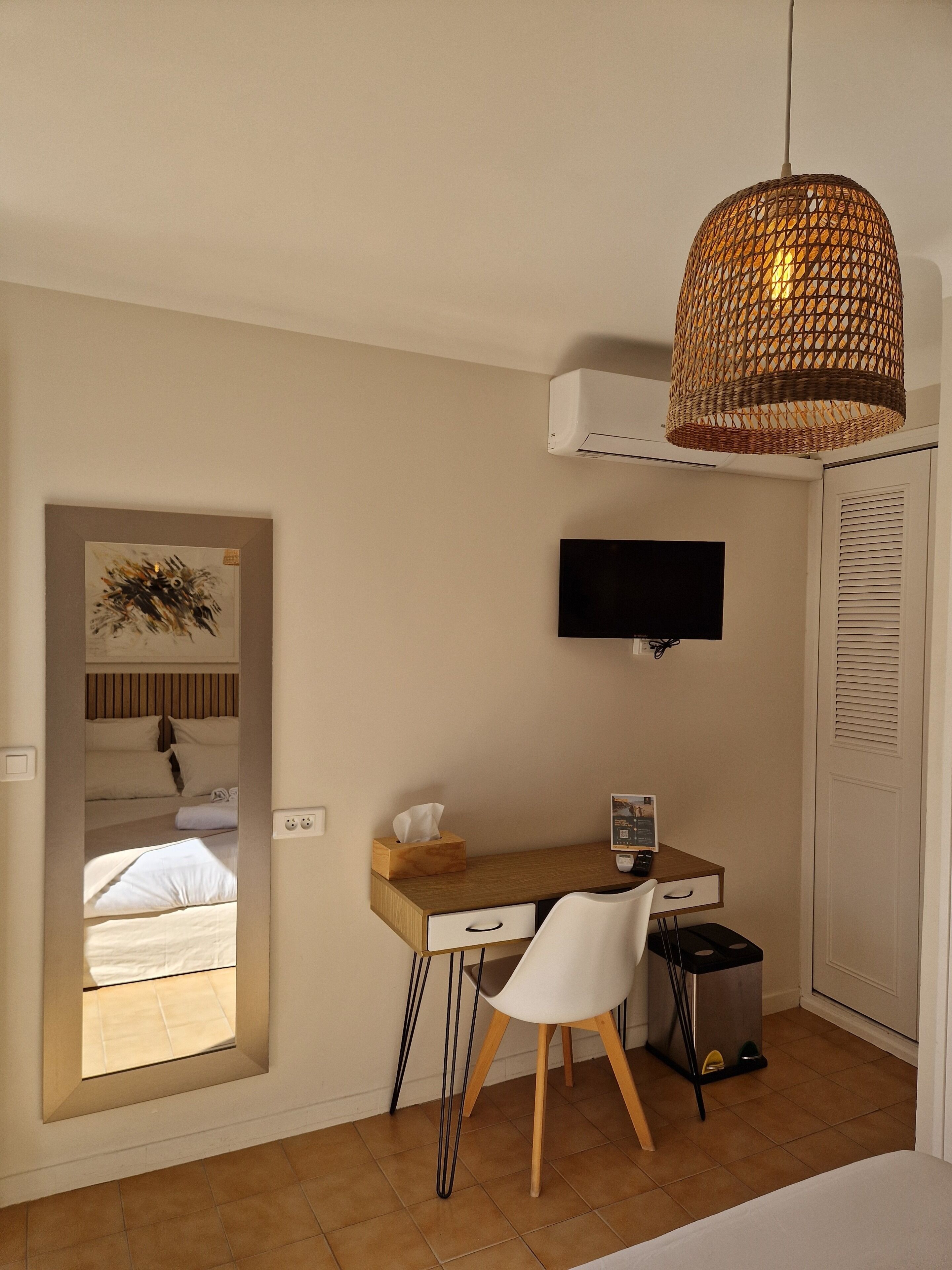 Un dormitorio con cama, escritorio con silla, televisor y lámpara colgante.