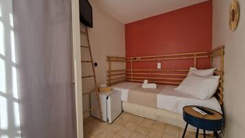 A small room with a bed, a small table, a ladder, and a television mounted on the wall.