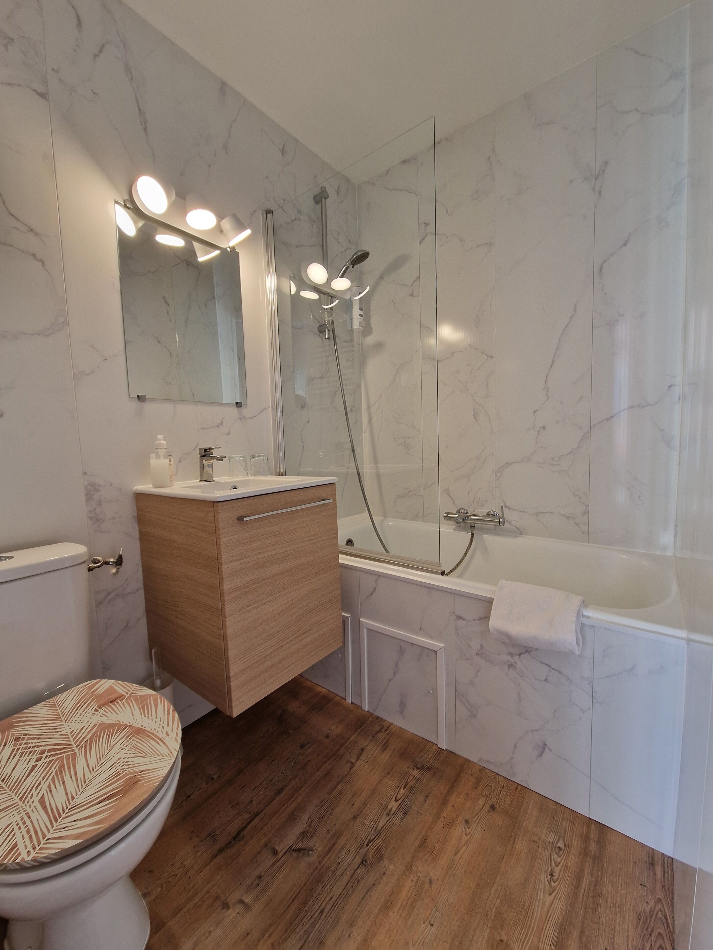 A bathroom with a toilet, wooden vanity, mirror, and a bathtub.