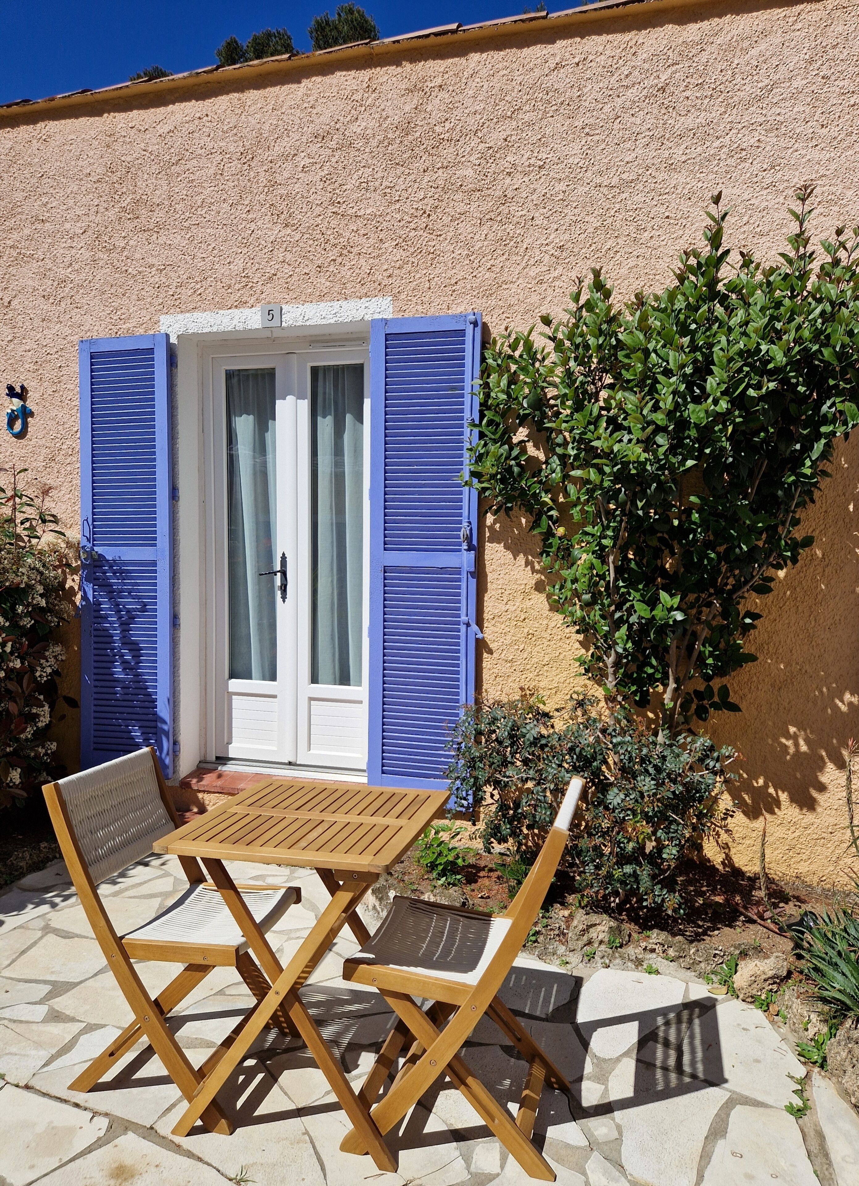 A patio with a table and chairs, a door with blue shutters, and a wall with a number '5'.