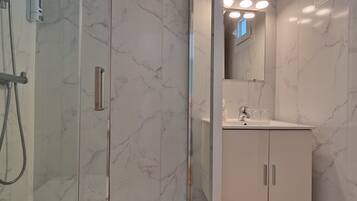 Un baño moderno con ducha de vidrio, un lavabo blanco y un espejo sobre el lavabo.