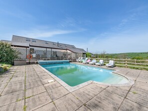 A swimming pool with lounge chairs, a fenced area, and a building with a sloped roof.