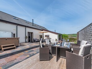 An outdoor patio with wicker furniture, a table set for dining, and a view of the countryside.