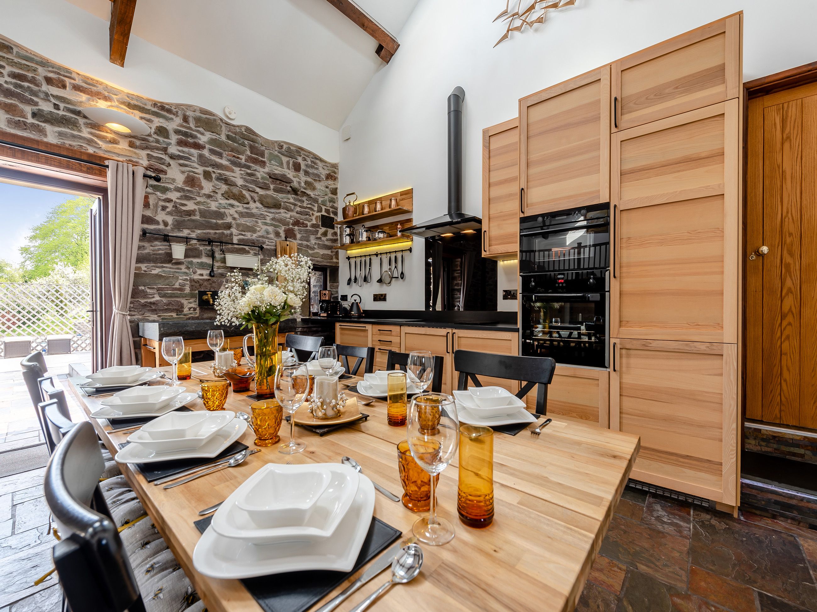 A dining area with a stone wall, wooden cabinets, and a long table set for a meal.