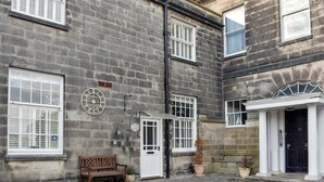 A building with a stone facade, multiple windows with shutters, a door, and a small bench outside. - 4 bedroom accommodation in Whitby (Whitby)