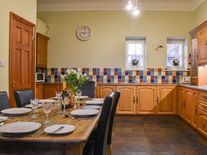 A dining area with a wooden table set for four, a clock on the wall, and a tiled backsplash. - 4 bedroom accommodation in Whitby (Whitby)