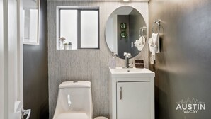 A modern bathroom with a toilet, a sink with a mirror, and a window. - Prime Location w King Accommodations Near Downtown (Austin)