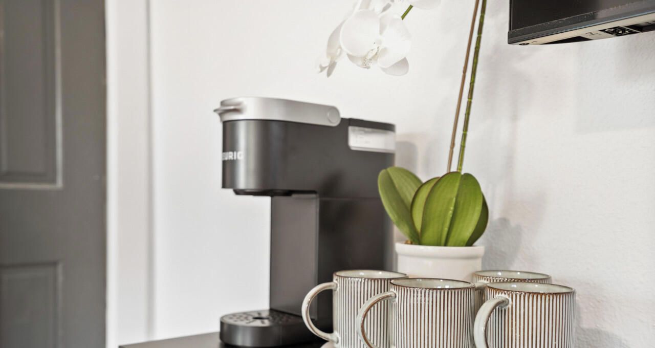 En kaffemaskine, to kopper og en potteplante på et bord.