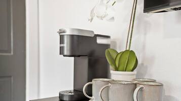 En kaffemaskine, to kopper og en potteplante på et bord.