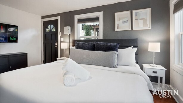A modern hotel room with a large bed, a ceiling fan, a TV displaying streaming services, and a window with a view. - Prime Location w King Accommodations Near Downtown (Austin)