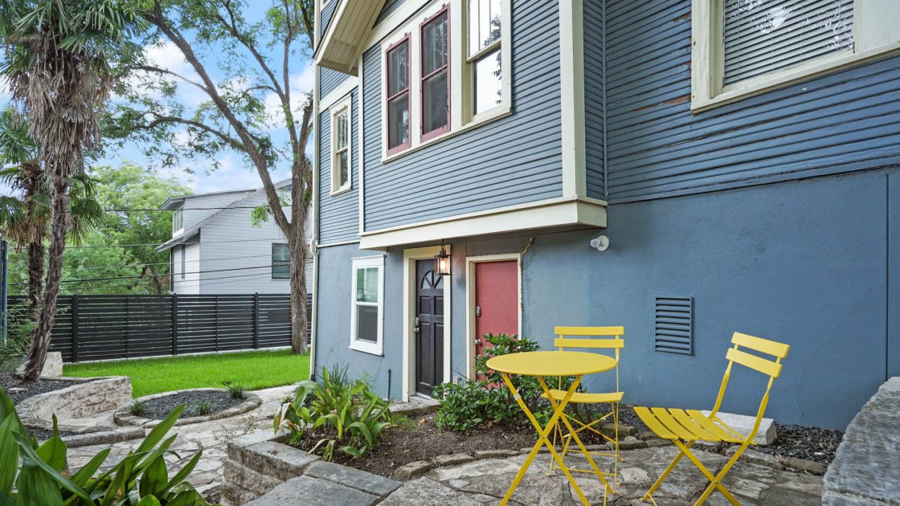 Una casa con facciata blu, una porta rossa e un piccolo patio con sedie gialle e un tavolo.