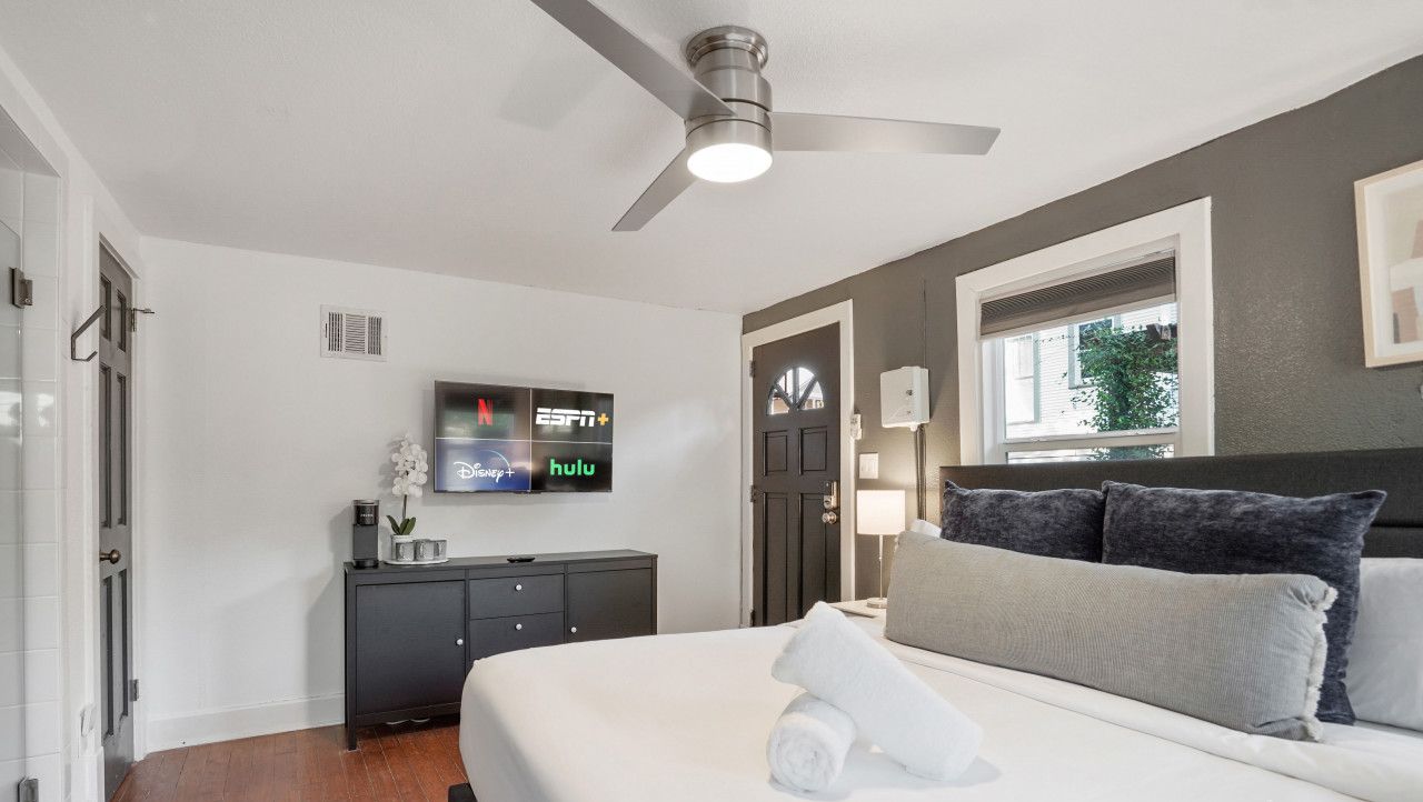 Ein modernes Hotelzimmer mit einem großen Bett, einem Deckenventilator, einem Flachbildfernseher, einer dunklen Holzkommode und einem Fenster mit Aussicht.