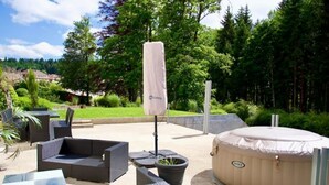 Een terras buiten met rieten meubilair, een jacuzzi en een overdekte parasol.