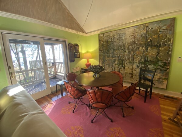 A dining area with a round table, six chairs, a red carpet, and a large abstract painting on the wall.