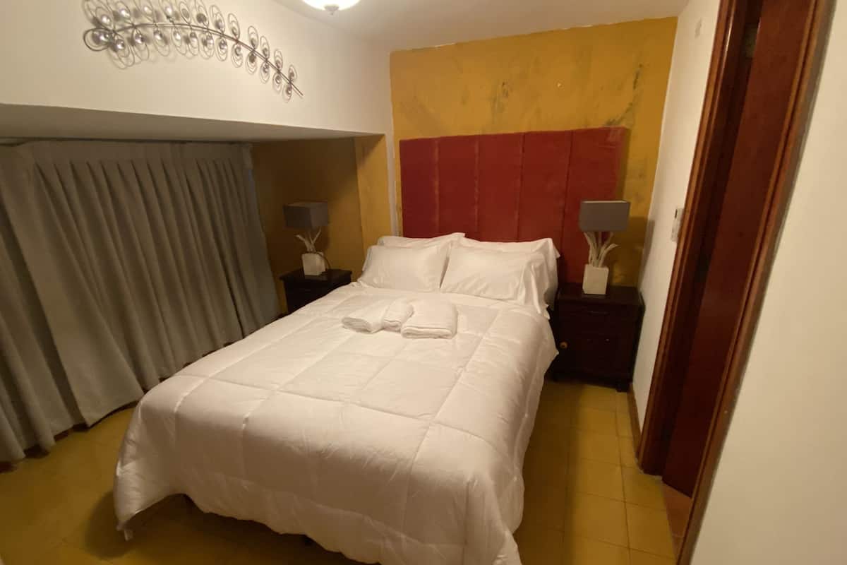 A neatly made bed with white linens, a red headboard, and two bedside tables with lamps.