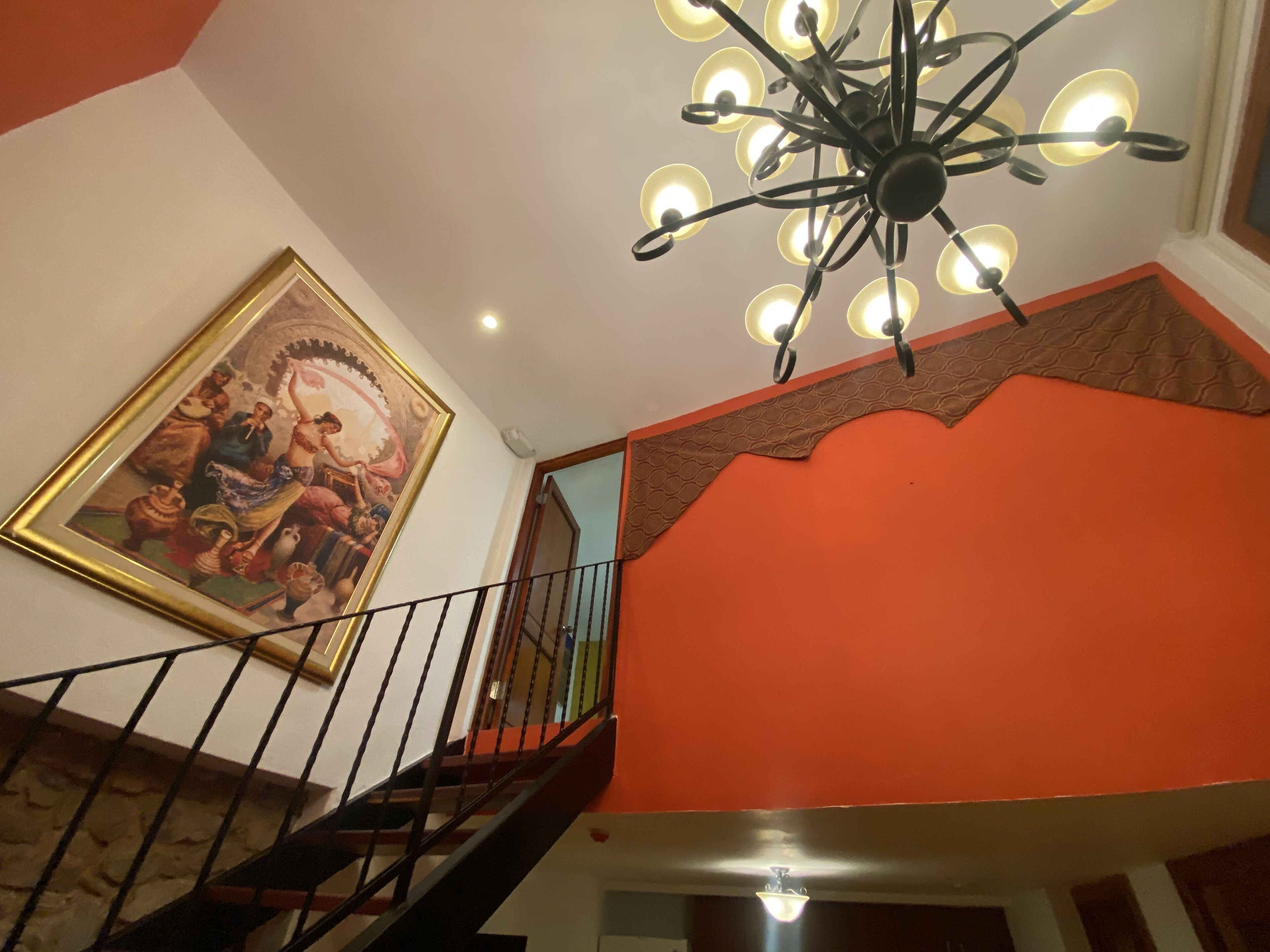 Uma escada com corrimão preto, um lustre no teto e um quadro na parede.