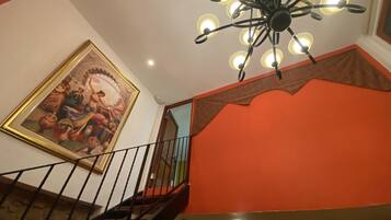 Uma escada com corrimão preto, um lustre no teto e um quadro na parede.